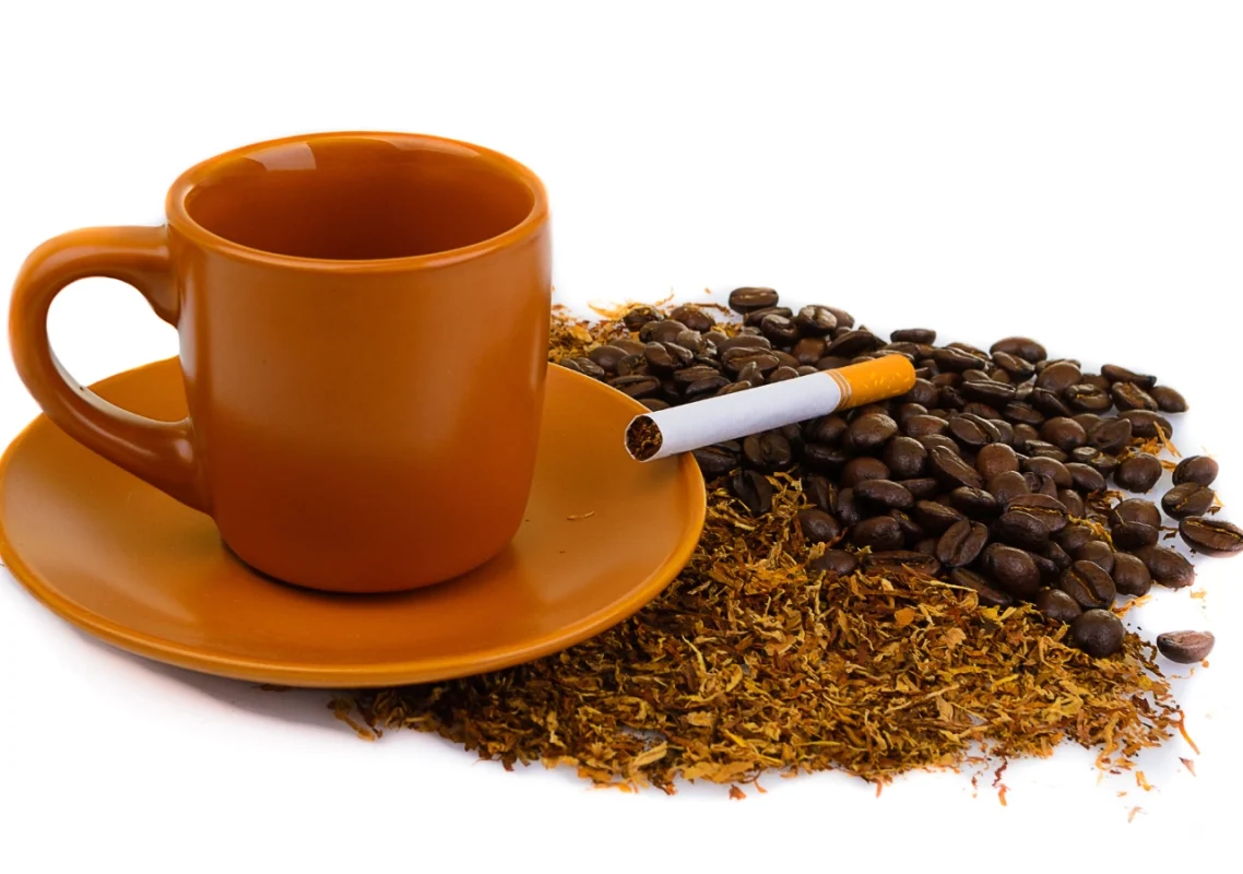 šoljica kafe i cigareta okruženi duvanom i zrnima kafe