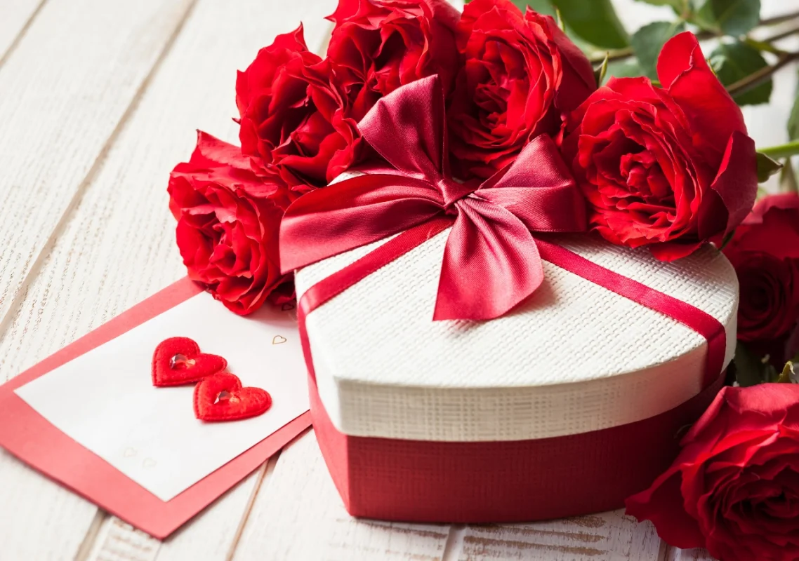 poklon za dan zaljubljnenih sa crvenom mašnom, ružama i čestitkom sa dva srca