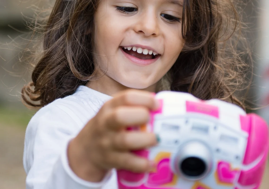 devojčica sa velikim osmehom gleda i igra se sa svojim digitalnim fotoaparatom za decu